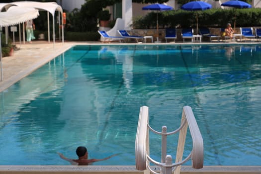 Ischia, Naples, Italy, About the July 2019. Man in the pool with green water. In the foreground, a white handrail.