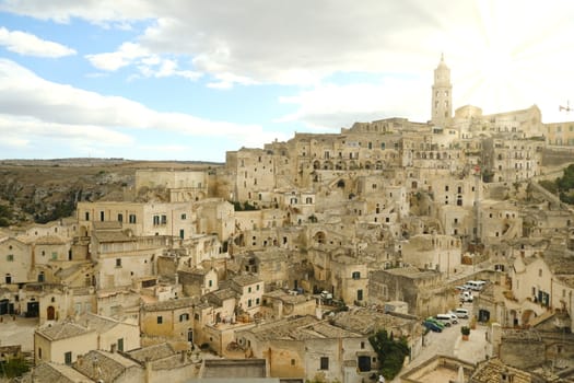 View of the city of Matera in Italy. Church with bell tower and houses built in beige tuff stone. Setting sun.