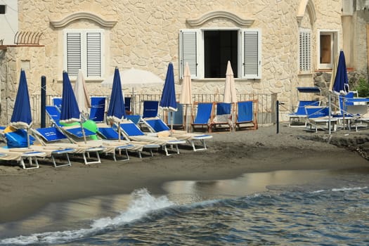 Ischia, Naples, Italy, About the July 2019. Stone house on the beach of the Mediterranean sea. Umbrellas and sun loungers on a small beach.