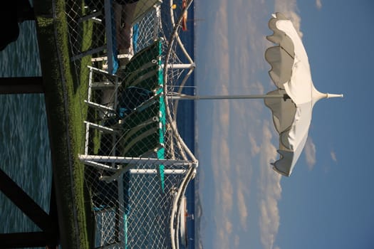 Ischia, Naples, Italy, About the July 2019.  Umbrella on a pier with a white parapet on the sea of Ischia. In the background a ferry boat.