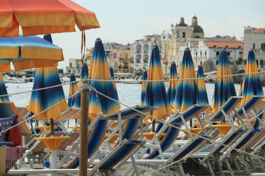 Umbrellas and deckchairs on the beach of Ischia Porto. In the background the Aragonese Castle.