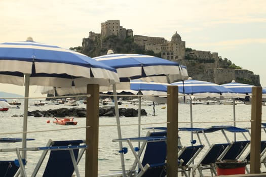 Umbrellas and deckchairs on the beach of Ischia Porto. In the background the Aragonese Castle.