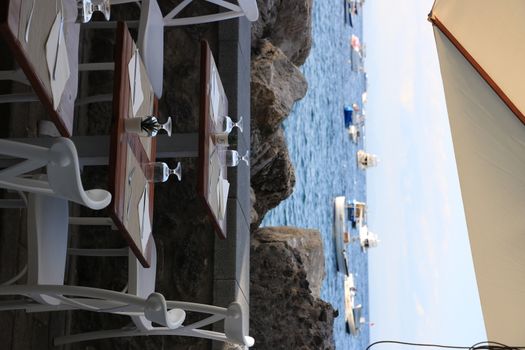 Ischia, Naples, Italy, About the July 2019. Umbrellas and tables of a romantic seaside restaurant. In the background the Aragonese Castle of Ischia.