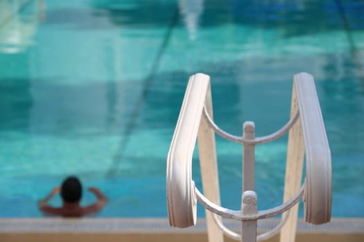 Man in the pool with green water. In the foreground, a white handrail.