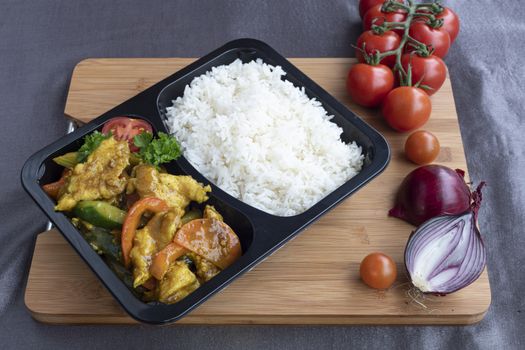 Box of stir fried chicken curry noodle served with white rice in a packaging recipient for take away