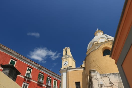 Procida island, Naples, Italy, About the July 2019. Church with bell tower and buildings in the square on the Island of Procida. Red and yellow painted facades.