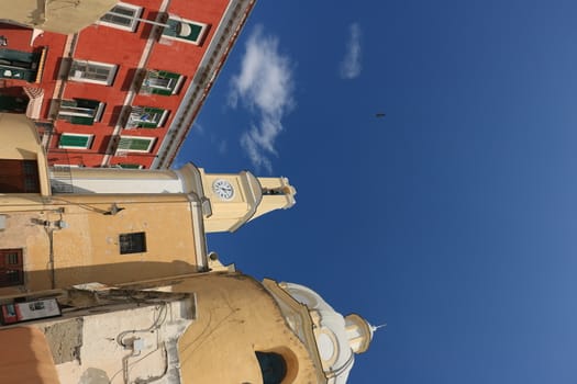Procida island, Naples, Italy, About the July 2019. Church with bell tower and buildings in the square on the Island of Procida. Red and yellow painted facades.