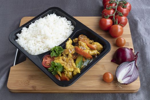 Box of stir fried chicken curry noodle served with white rice in a packaging recipient for take away