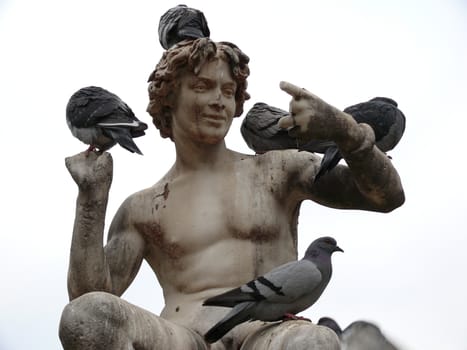 Sculpture of a boy with some pigeons huddled over.