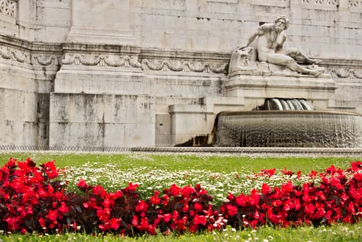 Altar of the Fatherland or Vittoriano in Piazza Venezia in Rome. Detail of a sculpture and a meadow with grass and red flowers.