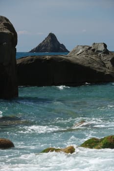 Waves of the sea break on the beach and on the rocks near the Cinque Terre. The waves break on the wild and natural beach with sheer mountains.