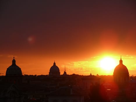 Rome, Lazio, Italy. Skyline with the setting sun over Rome's rooftops seen from the Caffarelli terrace. Church domes and city profile.