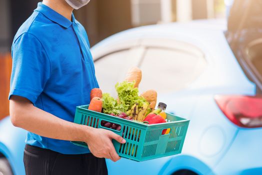 Asian grocery store delivery man wearing blue uniform and face mask protect he delivering fresh food vegetable in plastic box at door front home after coronavirus outbreak, back to new normal concept