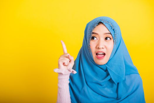 Asian Muslim Arab, Portrait of happy beautiful young woman Islam religious wear veil hijab funny smile she positive expression pointing with finger up to space isolated yellow background