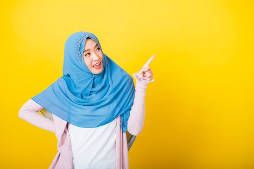 Asian Muslim Arab, Portrait of happy beautiful young woman Islam religious wear veil hijab funny smile she positive expression pointing finger side sideways to space isolated yellow background