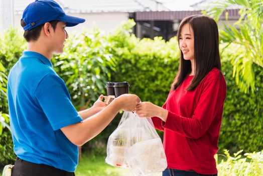 Asian young delivery man in blue uniform he making grocery service giving rice food boxes plastic bags to woman customer receiving front house under pandemic coronavirus, Back to new normal concept