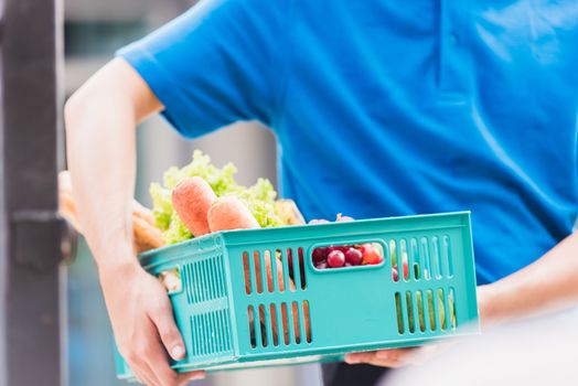 Asian grocery store delivery man wearing blue uniform and face mask protect he delivering fresh food vegetable in plastic box at door front home after coronavirus outbreak, back to new normal concept