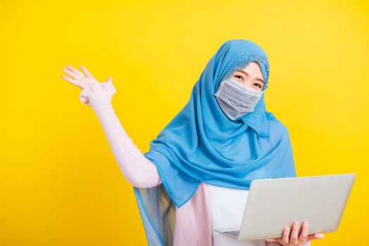 Asian Muslim Arab Portrait of happy beautiful young woman Islam religious wear veil hijab and face mask protect she quarantines disease coronavirus hold laptop computer and raise hand to indicate glad