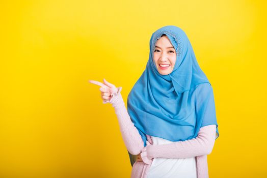 Asian Muslim Arab, Portrait of happy beautiful young woman Islam religious wear veil hijab funny smile she positive expression pointing finger side sideways to space isolated yellow background