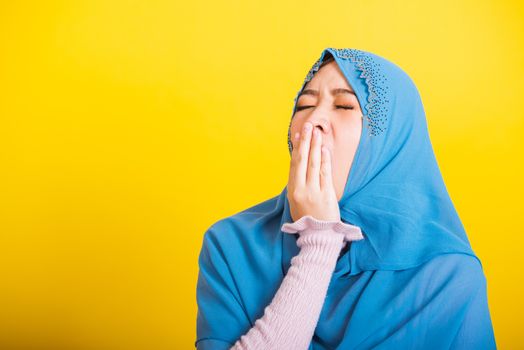 Asian Muslim Arab, Portrait of happy beautiful young woman Islam religious wear veil hijab funny she sleepy yawning wide open mouth hand cover mouth eyes closed studio shot isolated yellow background