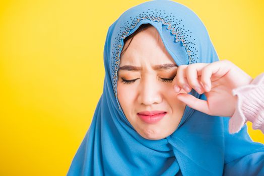 Asian Muslim Arab, Portrait of happy beautiful young woman religious wear veil hijab she sad crying using hand wiping tears in her eyes, studio shot isolated on yellow background with copy space