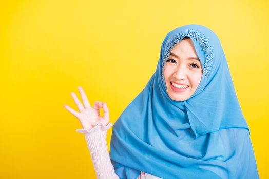 Asian Muslim Arab, Portrait of happy beautiful young woman Islam religious wear veil hijab funny smile she showing gesture fingers in okay gesture symbol, OK sign isolated yellow background