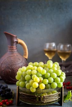 On the table in glass vase green grapes, near ceramic jug and two glasses guilt.