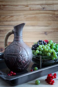 On the table, in a glass vase with green grapes next to a ceramic jug of wine. Presented on a wooden background. Copy space