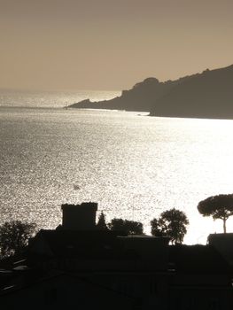 Silhouette of San Terenzo castle at sunset. Sky with clouds and sea of gold color.