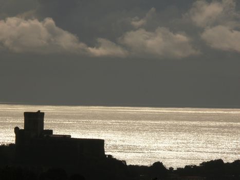 Silhouette of Lerici castle at sunset. Sky with clouds and sea of gold color.