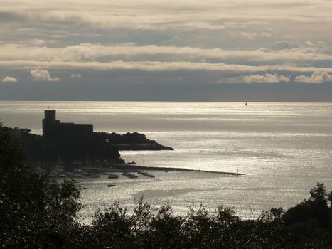 Silhouette of Lerici castle at sunset. Sky with clouds and sea of gold color.