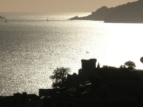 Silhouette of San Terenzo castle at sunset. Sky with clouds and sea of gold color.