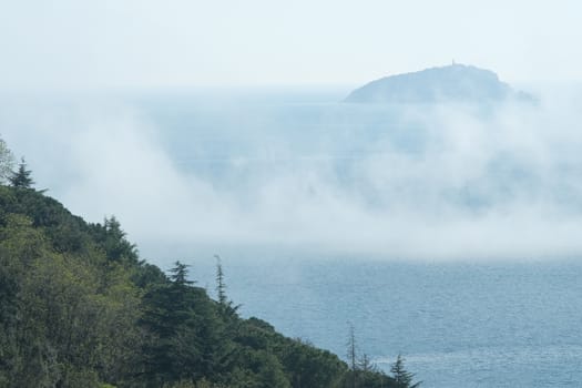 Low clouds over the Mediterranean sea with fog. Background with Tino island and hill with vegetation and trees. Lerici, near Cinque Terre, La Spezia, Italy.  