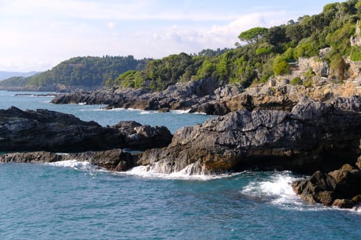 Cliff by the sea in the village of Tellaro di Lerici, near the Cinque Terre. Waves of the blue sea break on the rocks. Province of La Spezia.