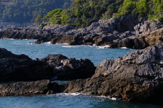 Cliff by the sea in the village of Tellaro di Lerici, near the Cinque Terre. Waves of the blue sea break on the rocks. Province of La Spezia.