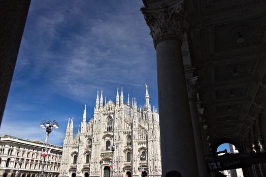 Milan, Lombardy, Italy, 04/27/2019. The facade of the cathedral with  blue sky. In the foreground the arches of the portico.