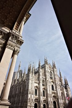 Milan, Lombardy, Italy, 04/27/2019. The facade of the cathedral with  blue sky. In the foreground the arches of the portico.