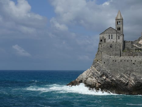 Church of San PIetro in Portovenere, built on a rock overlooking the sea. Sky with clouds and blue sea waves.