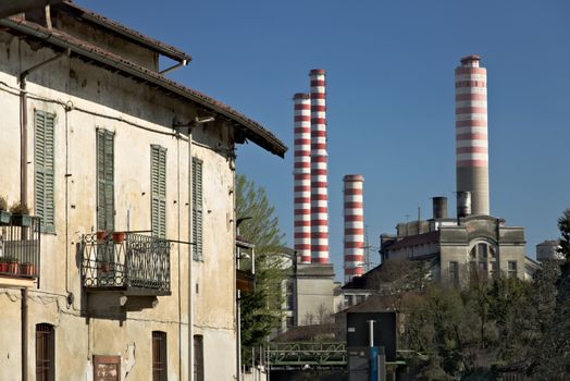 The industrial buildings and chimneys of the thermoelectric power plant located near the Naviglio Grande canal 40 km from Milan. In the foreground a traditional cascia that runs along the canal.