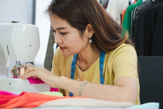 A senior female fashion designer from Asia is working in a textile factory. Confidently with starting a new business