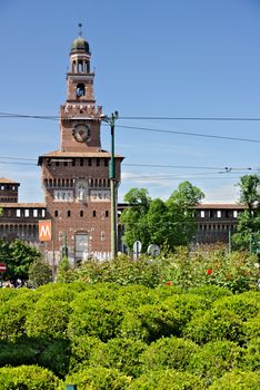 Milan, Lombardy, Italy, 04/27/2019. Sforza Castle in Milan. The tower above the main entrance.  In the foreground green bushes of the gardens.