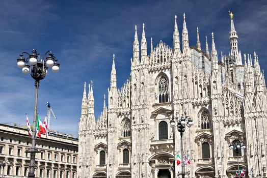 Milan, Lombardy, Italy, 04/27/2019. The facade of the cathedral. Flags waving on the blue sky.