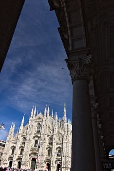 Milan, Lombardy, Italy, 04/27/2019. The facade of the cathedral with  blue sky. In the foreground the arches of the portico.