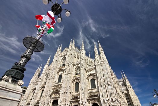 Milan, Lombardy, Italy, 04/27/2019. The facade of the cathedral. Flags waving on the blue sky.