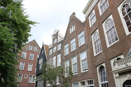 Amsterdam, Netherlands. About the July 2019. Begijnhof, the courtyard of the Beguines. In the city center a neighborhood with picturesque and old brick houses.  In the foreground statue of Jesus Christ.