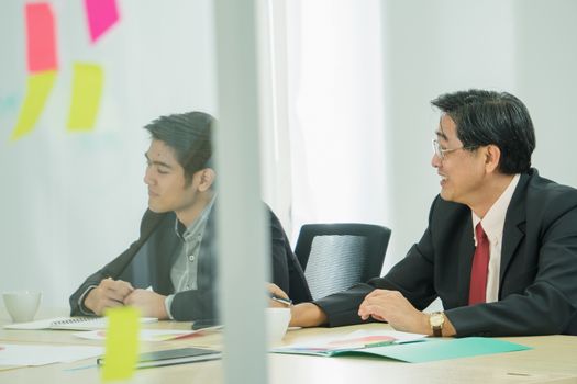 Asian businessmen are working and meeting together in their offices. They talk and smile at each other in a friendly manner.