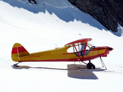 Jungfrau, Switzerland. A small yellow touring plane with red decorations on the snow of the Swiss mountains.