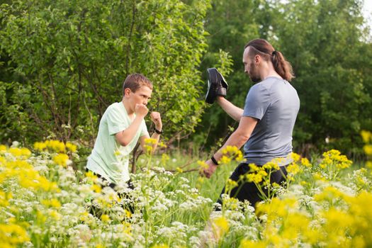 Father and son training to box in the park outdoors, fighting, care, sport, parenting, healthy lifestyle concept