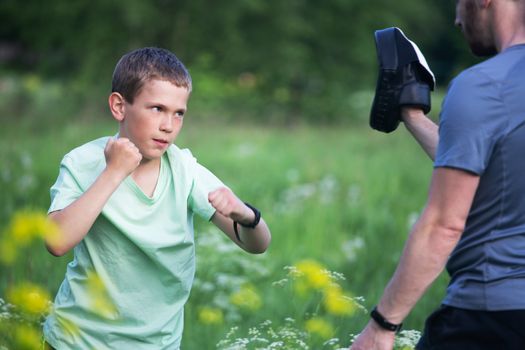 Father and son training to box in the park outdoors, fighting, care, sport, parenting, healthy lifestyle concept