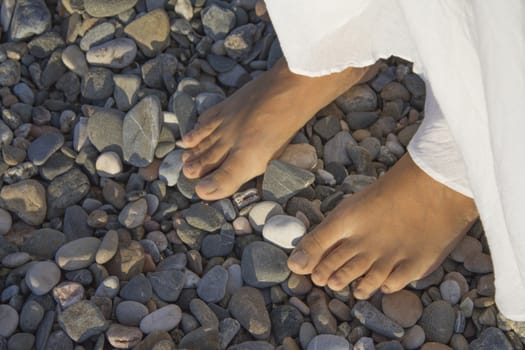 Feet of young woman on pebble beach. Part of a white skirt